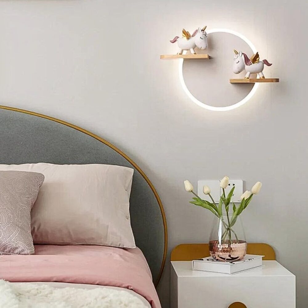 en el dormitorio de una niña con papel pintado gris, vemos una lámpara de pared redonda con dos pequeños unicornios dorados encima