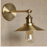 sobre una pared marrón claro se ve un aplique dorado de estilo industrial con una pantalla plana