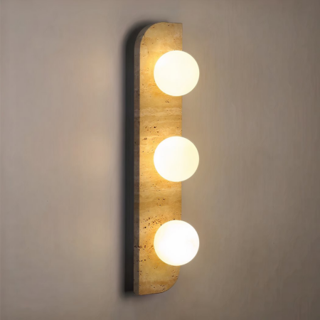 Aplique rectangular, redondeado en 2 esquinas opuestas, en piedra beige, con 3 bolas luminosas encendidas. Montado verticalmente en una pared marrón claro.