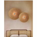 en un dormitorio con una pared gris sobre una cama de ratán, se ven dos apliques de mimbre de estilo japonés