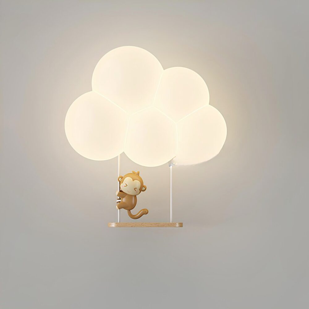 Aplique en forma de nube iluminada con un columpio debajo y un pequeño mono de dibujos animados colgando de la cuerda izquierda. El aplique está montado en una pared gris.