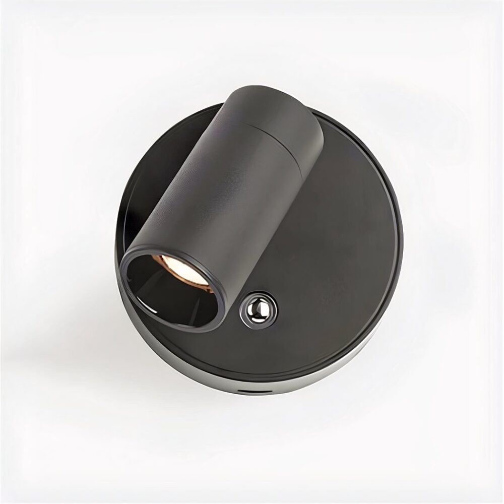 Aplique redondo negro con interruptor plateado bajo foco. Fondo blanco.