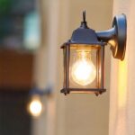 un aplique con forma de farol de exterior se ve encendido en una pared exterior