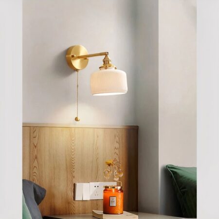 Aplique retro de cerámica con cadena de iluminación, en la versión de globo cuadrado con esquinas redondeadas, encendido y fijado a la pared de un dormitorio.