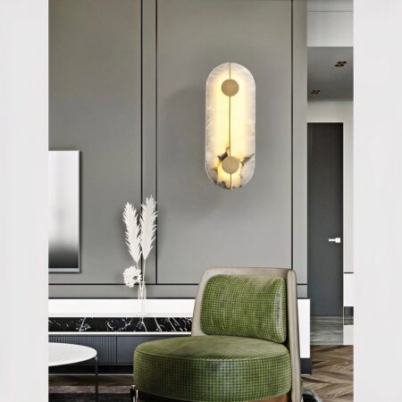 Aplique de mármol natural y latón colgado en la pared gris de un salón y colocado encima de un sillón verde bosque.