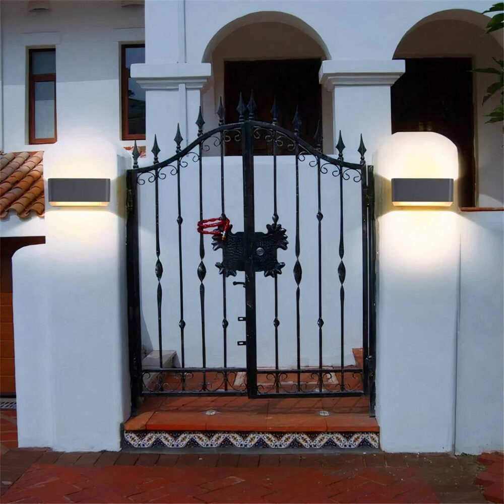 Aplique solar de diseño cuadrado fijado a la pared a ambos lados de una verja e iluminado.