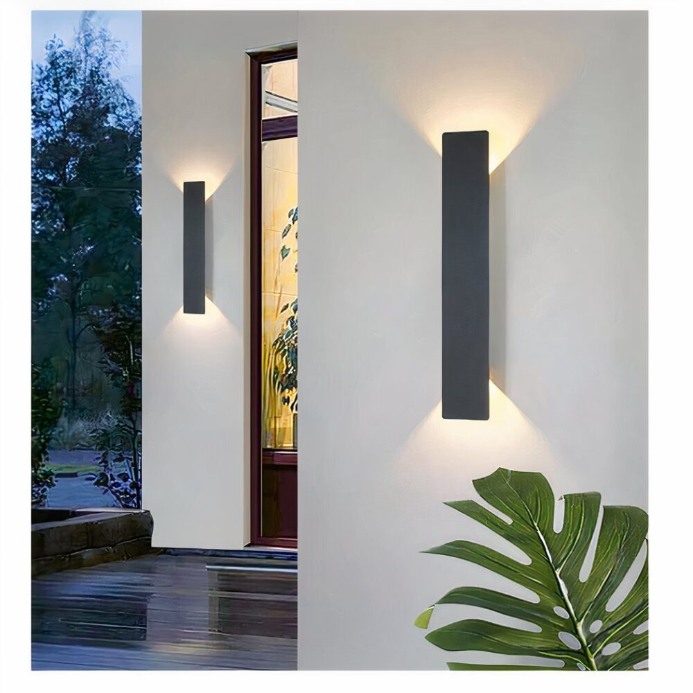 un aplique de exterior negro, rectangular, vertical y moderno se ve en una terraza sobre una pared blanca