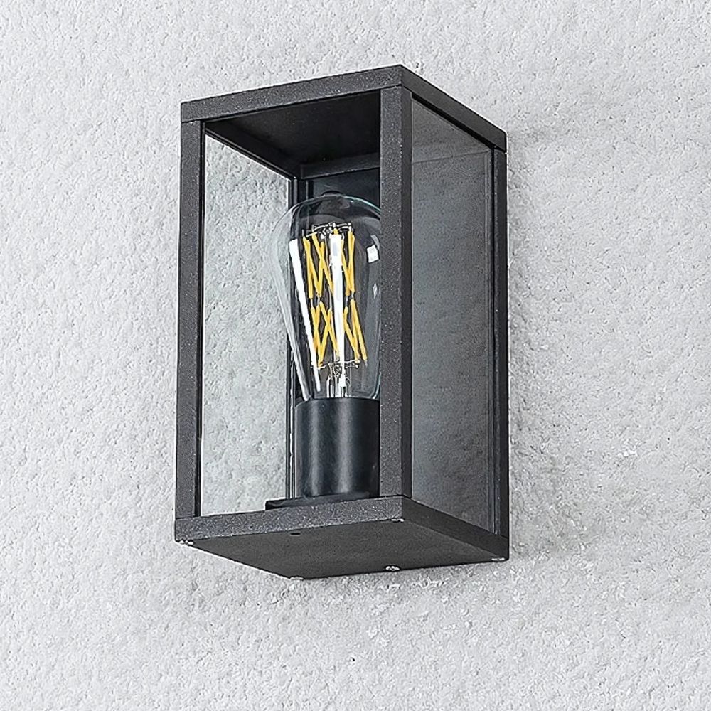 Aplique de exterior con bombilla visible en forma de caja con contornos de metal negro y con la bombilla apagada visible. Montado en una pared exterior blanca.